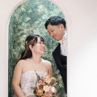 緑の植物柄の壁画を背にしたアーチ型ニッチで、見つめ合う新郎新婦。カラードレスで撮る前撮り