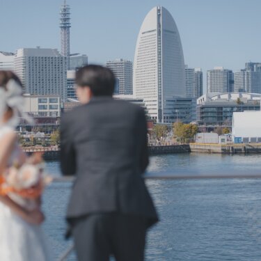 みなとみらいの観覧車とビル群を望む港を、並んで眺める新郎新婦の後ろ姿。横浜らしいロケーションフォト