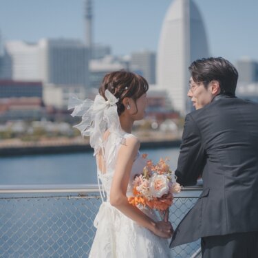 港を望む柵際で見つめ合う新郎新婦の後ろ姿。みなとみらいの街並みが広がるフォトウェディング
