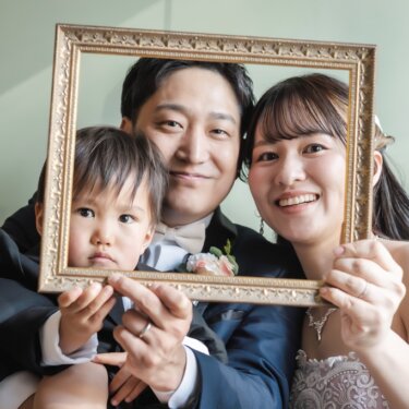 金の額縁を家族3人で持ち、フレームの中に顔を並べる家族写真。子どもと一緒に撮るスタジオフォト