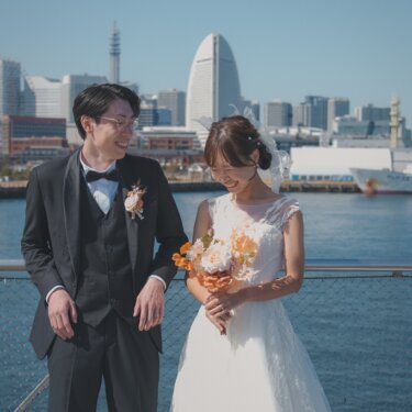 みなとみらいのランドマークタワーを望む柵際で、ブーケを見つめる新郎新婦を正面から写した前撮り