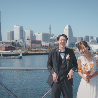 横浜ランドマークタワーと赤レンガ倉庫を望む大さん橋の柵際で、大笑いする新郎新婦のロケーションフォト