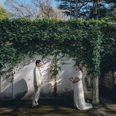 蔦に覆われた石造りの門の前で、離れて向かい合う新郎新婦。港の見える丘公園の緑が美しいロケーションフォト