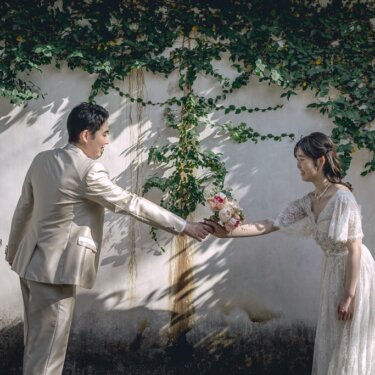 蔦の絡まる壁の前で、新郎が花嫁にブーケを手渡す演出ショット。プロポーズのようなシーンを残すフォトウェディング