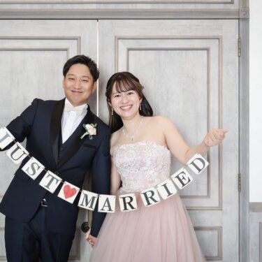 大きな木製の扉の前で『JUST MARRIED』のガーランドを掲げる、新郎新婦の笑顔のスタジオフォト