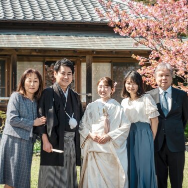 桜と古民家を背に、両家の家族と並ぶ白無垢の花嫁と紋付袴の新郎。横溝屋敷で撮る前撮りの家族写真