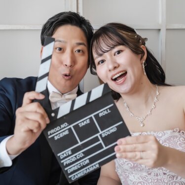 カチンコを一緒に持っておどける新郎新婦。ピンクのカラードレスで撮る遊び心あるスタジオフォト
