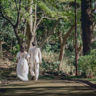 港の見える丘公園の緑豊かな小道を歩く新郎新婦の後ろ姿。レースのドレスの裾が揺れる結婚写真