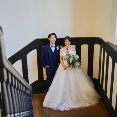 横浜市開港記念会館の階段を上から見下ろし、踊り場に並ぶ新郎新婦を写した引きの構図の前撮り