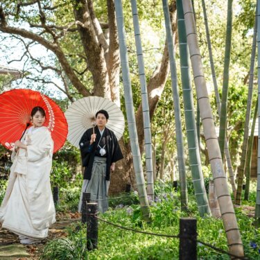 竹林の小道で朱赤の和傘を差す白無垢の花嫁と、白い和傘を持つ新郎。横溝屋敷の庭で撮る和装ロケーションフォト