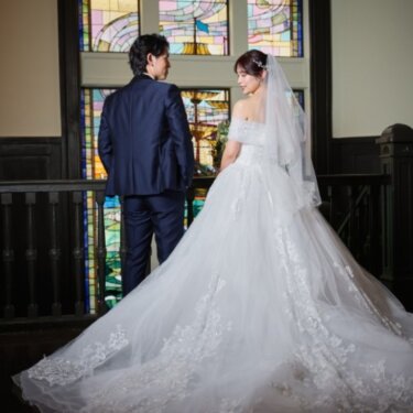 色鮮やかなステンドグラスの前に立つ新郎新婦の後ろ姿。長いトレーンが美しいバックスタイルの結婚写真