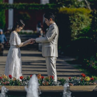 噴水とチューリップの花壇がある庭園で手を取り合う新郎新婦。春の港の見える丘公園で撮るウェディングフォト