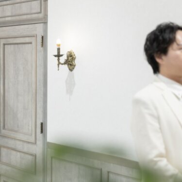 扉のすき間から顔を出す花嫁と、待つ新郎。映画のようなファーストミートの演出で撮るスタジオフォト