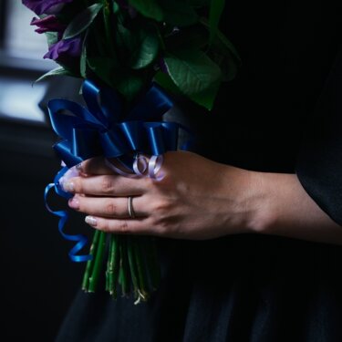 青いリボンで束ねた紫と白のブーケと、指輪が光る花嫁の手元のクローズアップの結婚写真