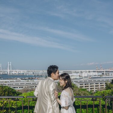ベイブリッジを望む展望台の柵際で、新郎が花嫁の額にキスをするやさしいシーン。港の見える丘公園の前撮り