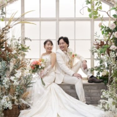 花のアーチ窓のセットに並んで腰かけ、マーメイドドレスのトレーンを広げた花嫁と新郎の結婚写真