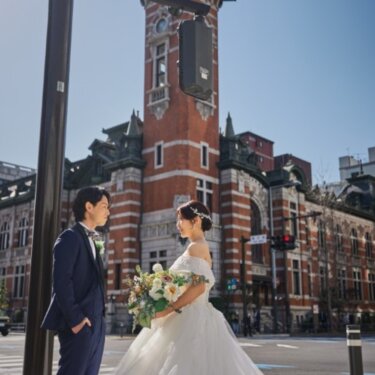 横浜市開港記念会館の赤レンガの時計塔を望む日本大通りの交差点で、見つめ合う新郎新婦の前撮り