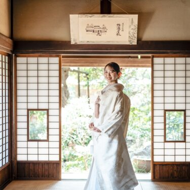 障子を開け放った座敷に立つ白無垢の花嫁のソロショット。裾を広げた古民家の和装フォトウェディング