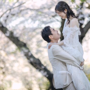 満開の桜を背景に、新郎が花嫁を抱き上げて見つめ合うダイナミックなポーズ。レースのドレスで撮る結婚写真