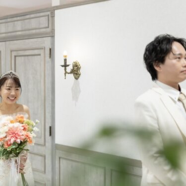 扉から出てきてほほえむ花嫁と、前を向いて待つ新郎を少し引きで写したファーストミートの前撮り