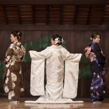 白無垢の袖を大きく広げて見せる花嫁を、両脇から家族の女性2人が見つめる家族写真入りの和装前撮り