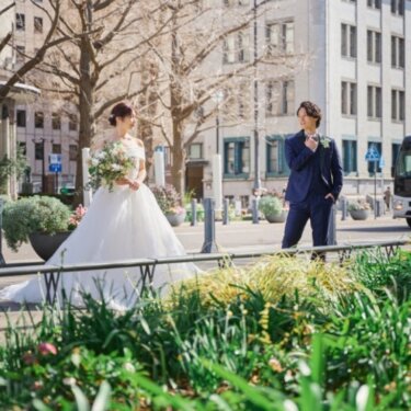 緑の花壇を前景に、日本大通りの街並みで離れて立つ新郎新婦を写したウェディングフォト