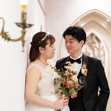 ゴシック調のアーチ扉と真鍮の壁灯を背景に、ブーケを持って見つめ合う新郎新婦。横浜のスタジオで撮る洋装フォトウェディング
