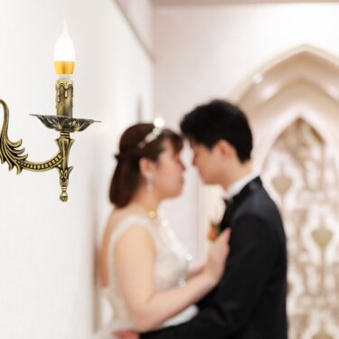 真鍮の壁灯にピントを合わせ、奥で額を寄せる新郎新婦をぼかしたスタジオフォト。アーチの装飾が映える結婚写真