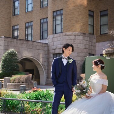 日本大通り沿いの歴史的な近代建築を望む花壇の前で、見つめ合う新郎新婦。横浜の街ロケで撮る前撮り