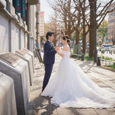 日本大通りの並木道で両手を合わせて見つめ合う新郎新婦。ボリュームのあるウェディングドレスが映える横浜の前撮り