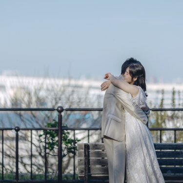 ベイブリッジを望む展望台の柵の前で抱き合う新郎新婦。港の景色と青空が広がる横浜のロケーションフォト