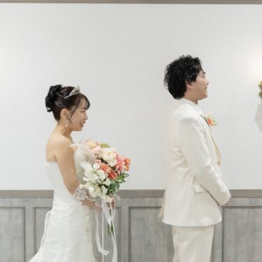 壁灯の並ぶ部屋で、背を向けて待つ新郎に近づくブーケの花嫁。ファーストミート直前のスタジオフォト