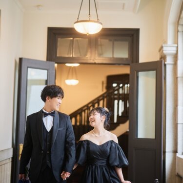 横浜市開港記念会館の入口で、手をつないで見つめ合う新郎新婦。奥に曲線の階段が見えるウェディングフォト