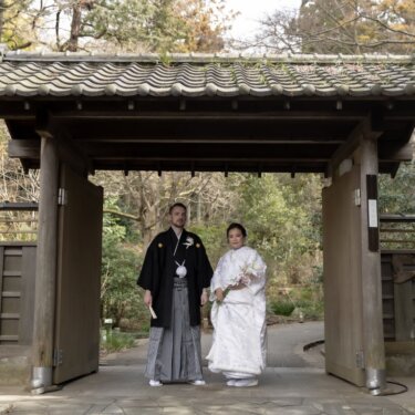 久良岐能舞台の瓦屋根の門の下に並んで立つ、白無垢の花嫁と紋付袴の新郎の和装前撮り