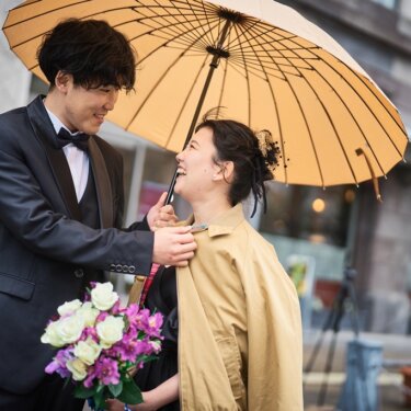新郎が大きな和傘を差し、花嫁にコートを羽織らせるやさしいしぐさ。雨の日のフォトウェディング