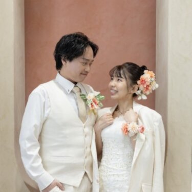 テラコッタ色の壁のニッチで、ジャケットを羽織ったウェディングドレスの花嫁が新郎を見つめるスタジオフォト