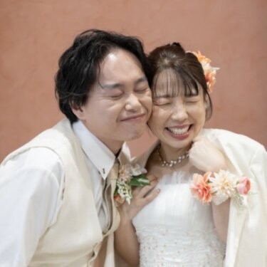 テラコッタ色の壁の前で頬を寄せ合い、目を閉じて笑う新郎新婦。仲の良さが伝わるスタジオフォト