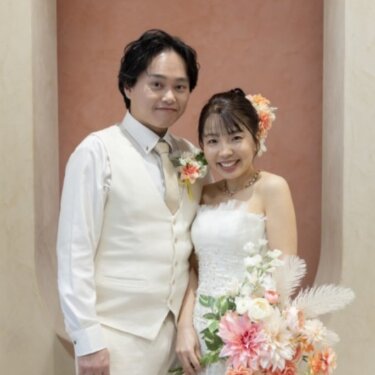テラコッタ色の壁を背景に、白いベストの新郎とマーメイドドレスの花嫁がほほえむ正面の結婚写真