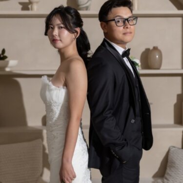 アーチ型のニッチと竹の照明のセットで、背中合わせに立つタキシードの新郎とマーメイドドレスの花嫁のスタジオフォト
