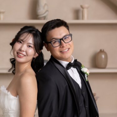アーチの棚のセットで背中合わせになり、カメラに笑顔を向ける新郎新婦のスタジオ前撮り