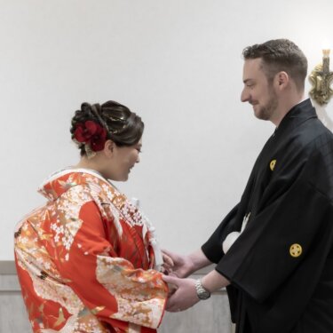 両手を取り合ってほほえむ色打掛の花嫁と紋付袴の新郎。落ち着いたファーストミートの和装フォトウェディング