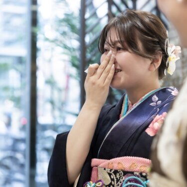 紺の振袖の女性が涙をぬぐう感動の瞬間。色打掛の花嫁の支度を見守る、和装前撮りの日の家族のスナップ