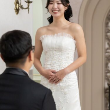 片膝をつく新郎の後ろ姿越しに、ほほえむウェディングドレスの花嫁を写したプロポーズ演出の前撮り
