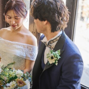 横浜開港記念会館にて、窓辺のやわらかな光の中で、ブーケを見つめる花嫁と新郎のアップ。オフショルダーのドレスで撮る結婚写真
