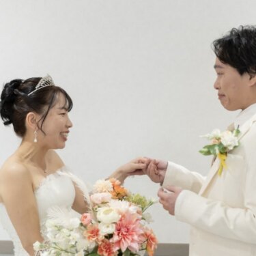 新郎が花嫁の手をやさしく取り、見つめ合う瞬間。ピンクのダリアのブーケが映えるウェディングフォト