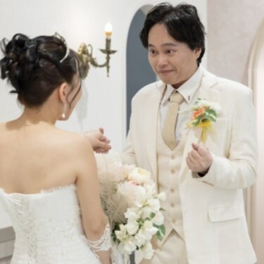 花嫁の背中越しに、驚いて照れ笑いする白いタキシードの新郎の表情を写したファーストミートの前撮り