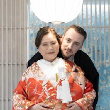 丸い和紙の照明の下で、後ろから新郎に抱きしめられてほほえむ赤い色打掛の花嫁。スタジオで撮る和装前撮り