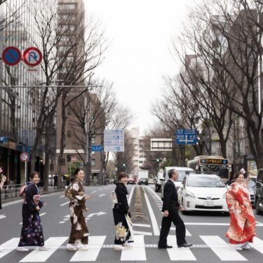 大さん橋への道路標識が見える横浜の街並みで、国旗を掲げた新郎と家族全員が横断歩道を渡るユニークな前撮り