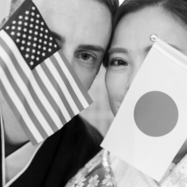 アメリカと日本の国旗を顔の前に掲げて顔を隠す新郎新婦をモノクロで写した、国際結婚を象徴する結婚写真