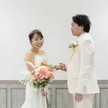 壁灯のある白い壁の前で、大笑いする花嫁と手をつなぐ新郎。ファーストミート直後のウェディングフォト